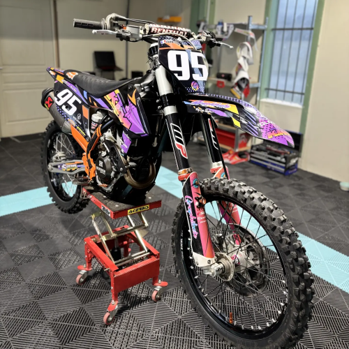 Moto cross KTM habillée d'un kit déco violet, orange et noir, vue trois-quarts avant