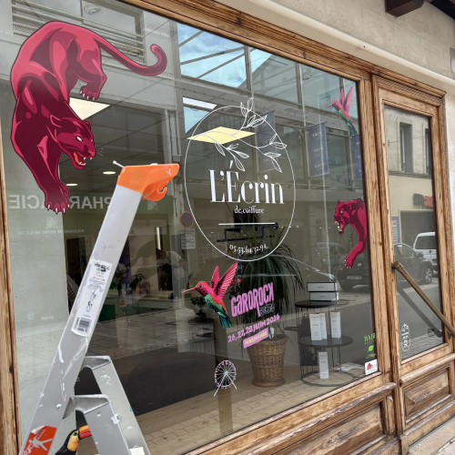 Pose d'une vitrophanie décorative avec panthères roses sur la vitrine de L'Écrin
